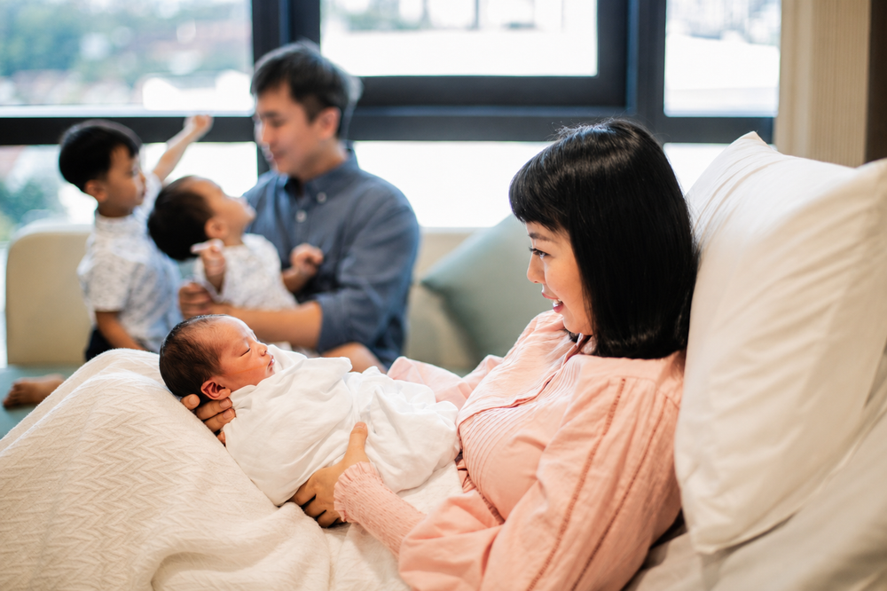 Asian mother holds newborn while father bonds with two older children.