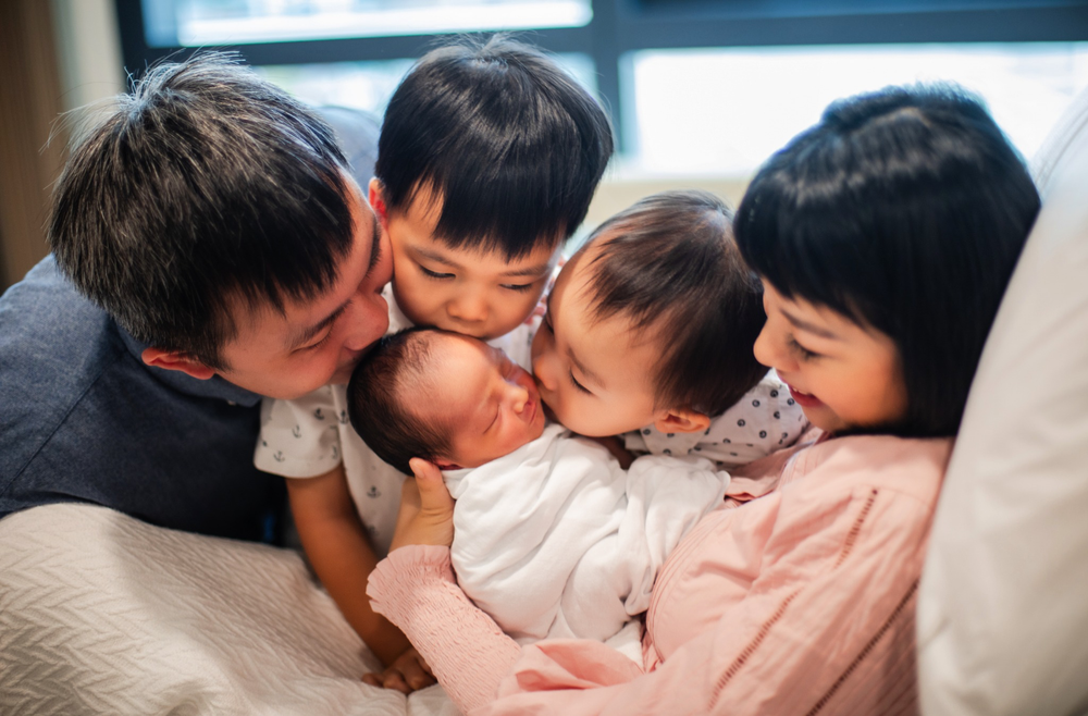 Loving Asian family of five sharing tender moment with newborn baby.