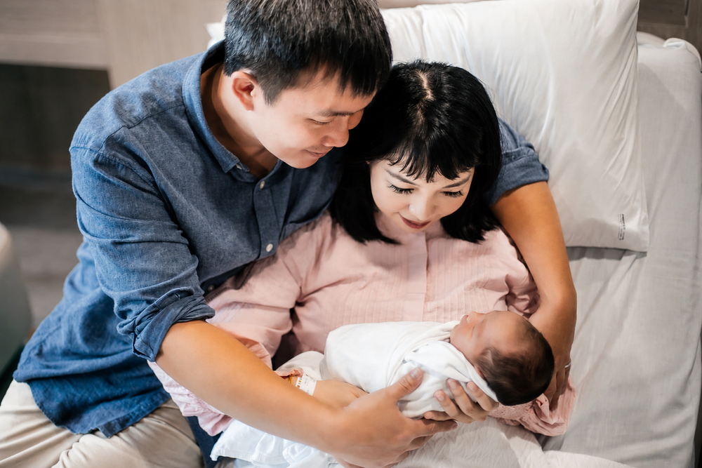 Asian parents sharing a tender moment with their newborn in hospital.