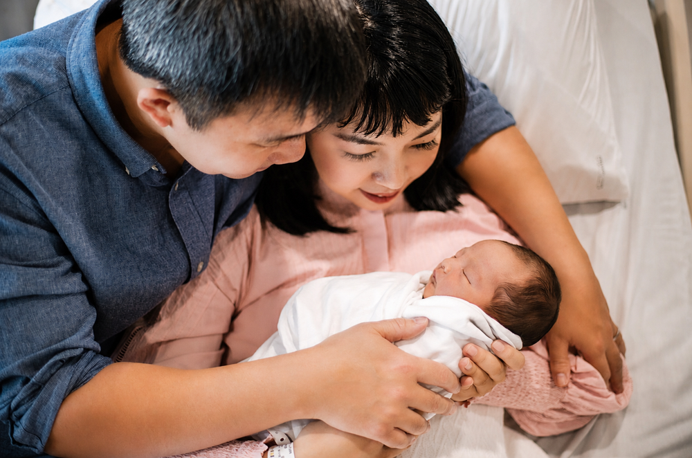 New parents tenderly gaze at their swaddled newborn baby together.