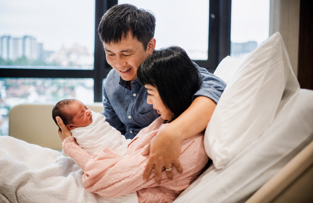 Happy Asian couple in hospital room smiling at their newborn baby.