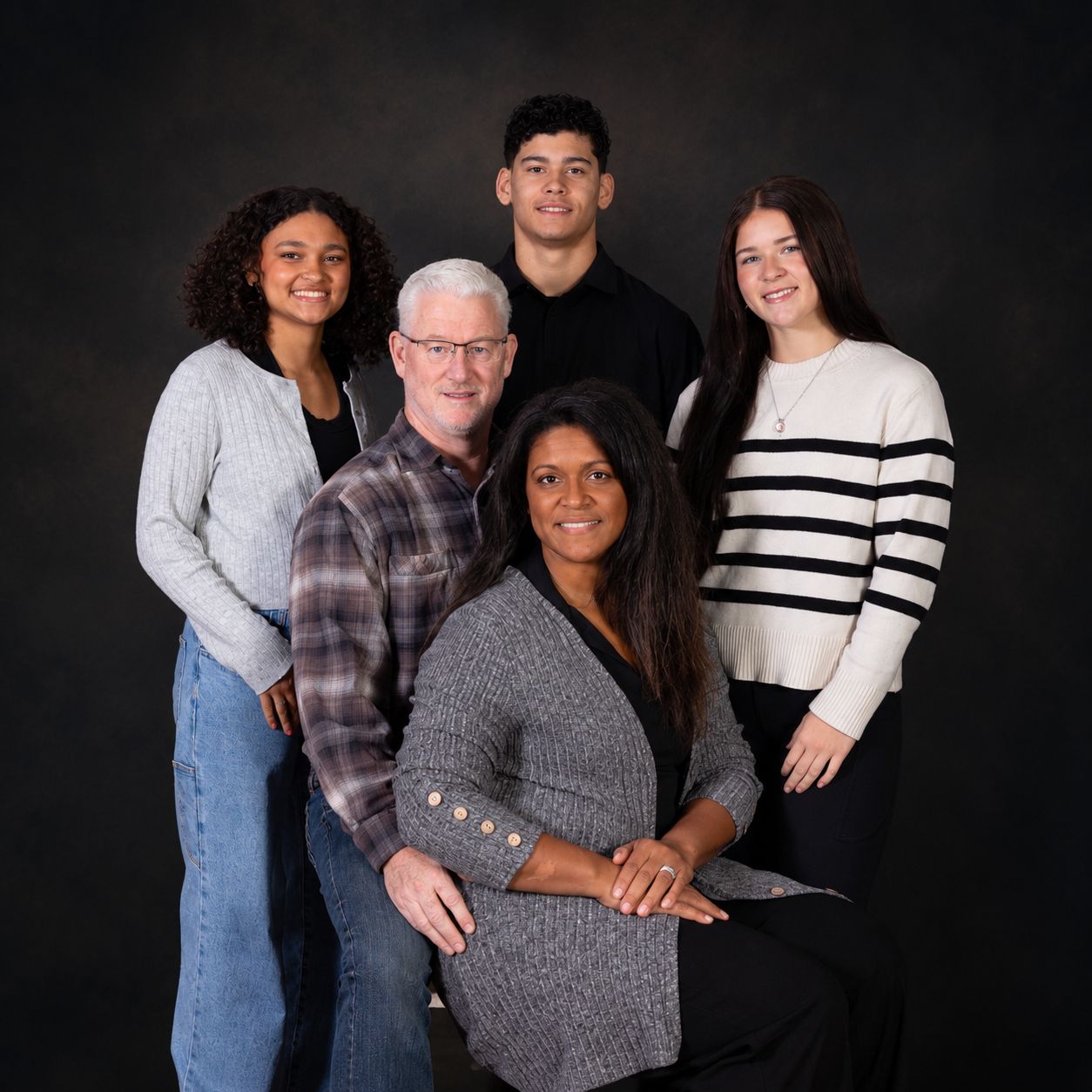 Family of five posing for a professional portrait against a dark studio background, smiling warmly together.