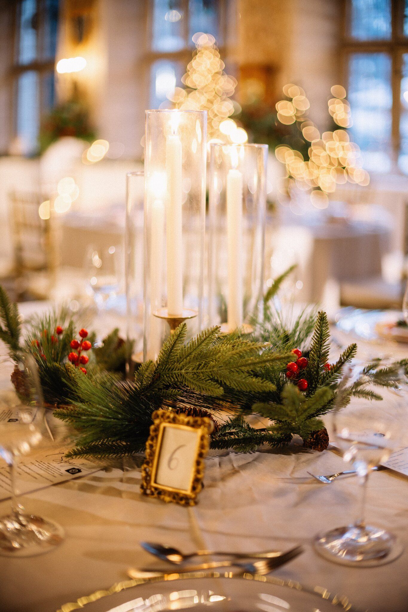 Taper candles, pine and red berry centrepiece with a gold table number at a Banff Christmas wedding reception