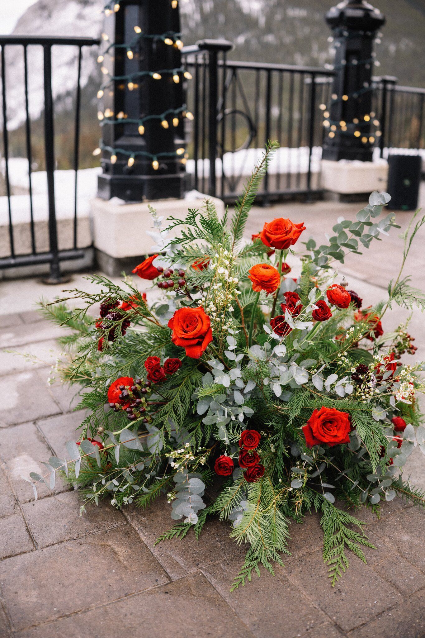 Red rose, cedar and eucalyptus ceremony arrangement beside lamp posts wrapped in string lights at the Fairmont Banff Springs