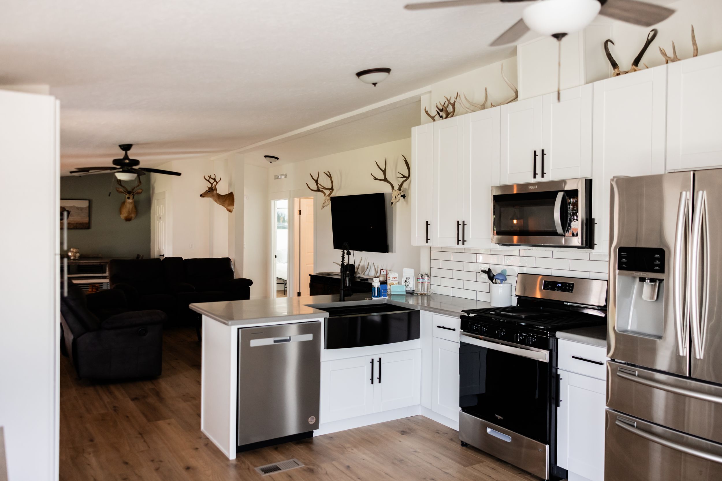 Open-concept kitchen with white cabinets, stainless steel appliances, and a breakfast bar overlooking a cozy living room with antler decor.