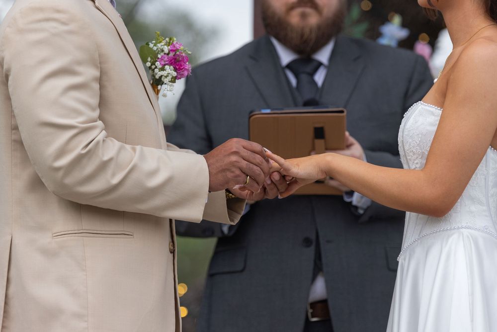 Bride and groom hold hands while exchanging vows during an outdoor wedding ceremony as the officiant stands behind them holding a book.