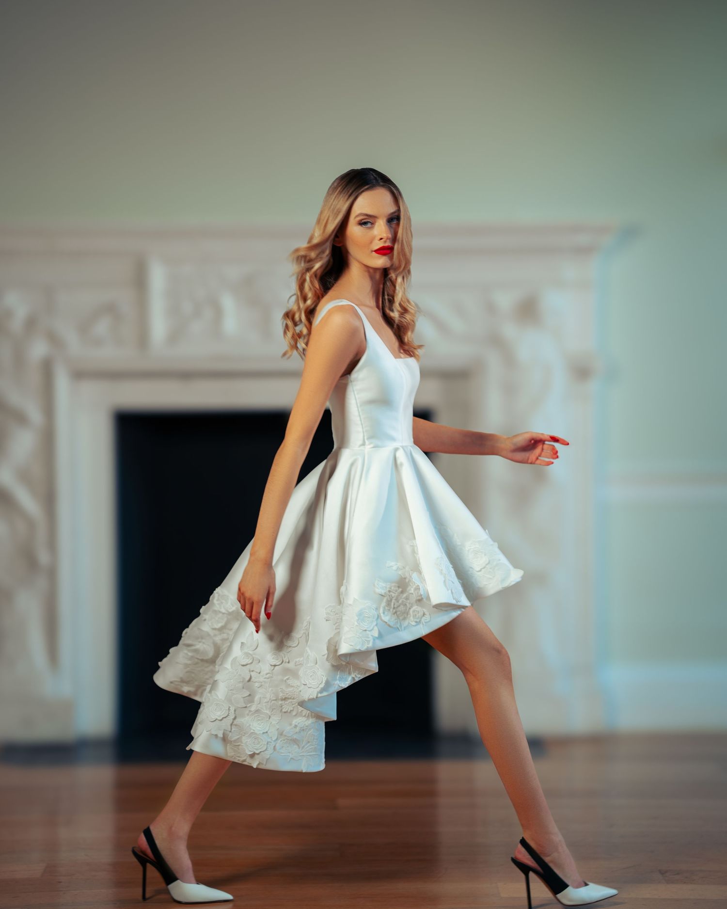 Artistic bridal portrait showing flowing white dress in motion against light blue walls.
