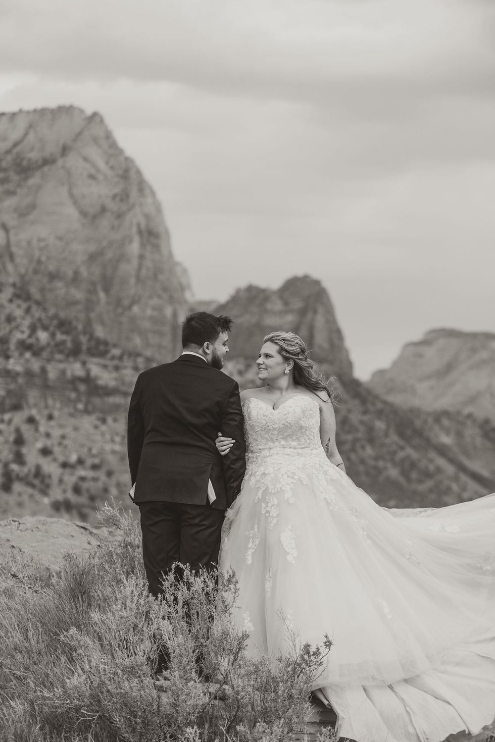 Black and white photo of a bride and groom sharing a romantic moment with stunning mountain cliffs in the background.