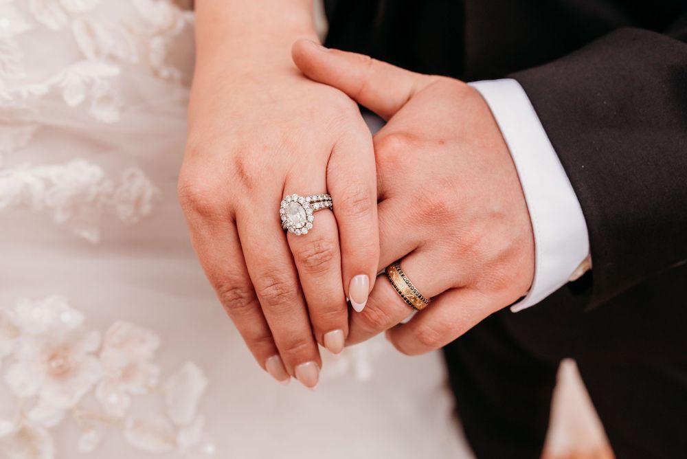 Close-up of couple's hands showing diamond engagement ring and gold wedding band on wedding day.