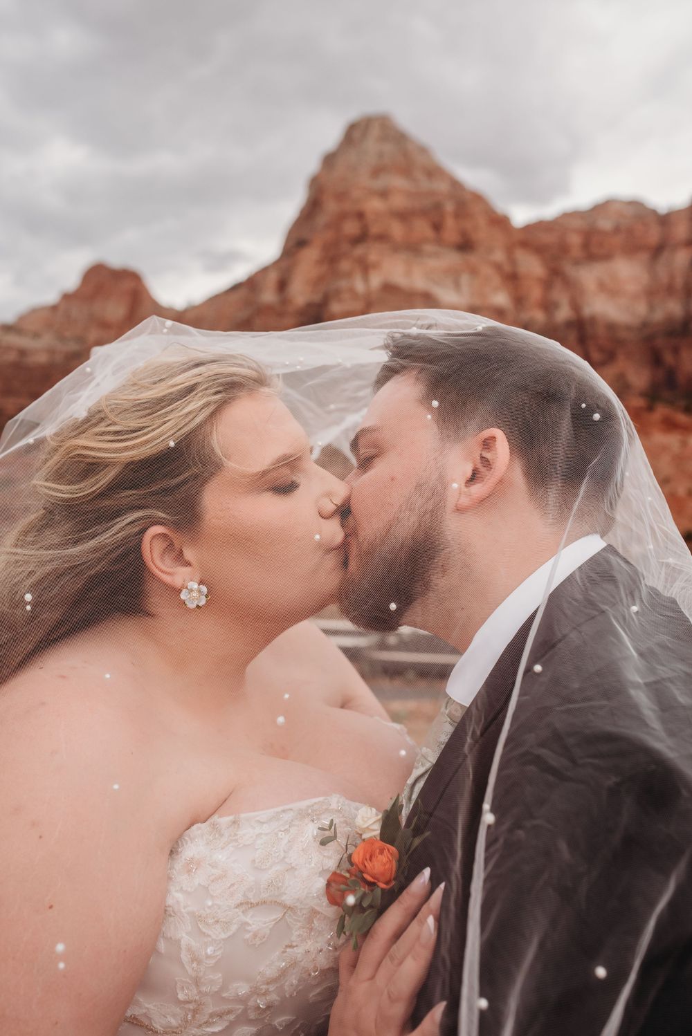 Bride and groom sharing a romantic kiss under a wedding veil with red rock formations in the background.