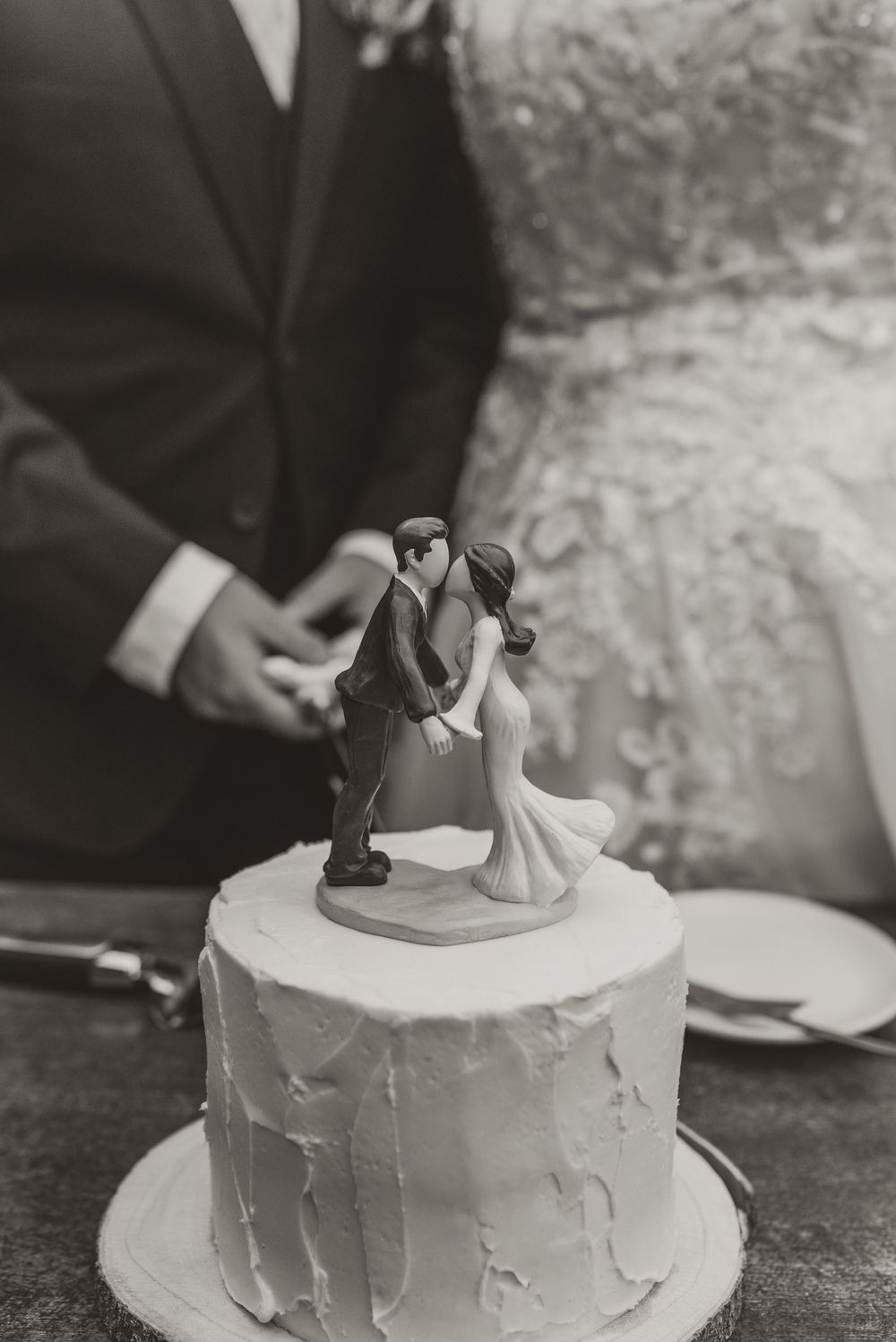 Black and white photo of a wedding cake topper featuring a kissing bride and groom figurine on a white frosted cake.
