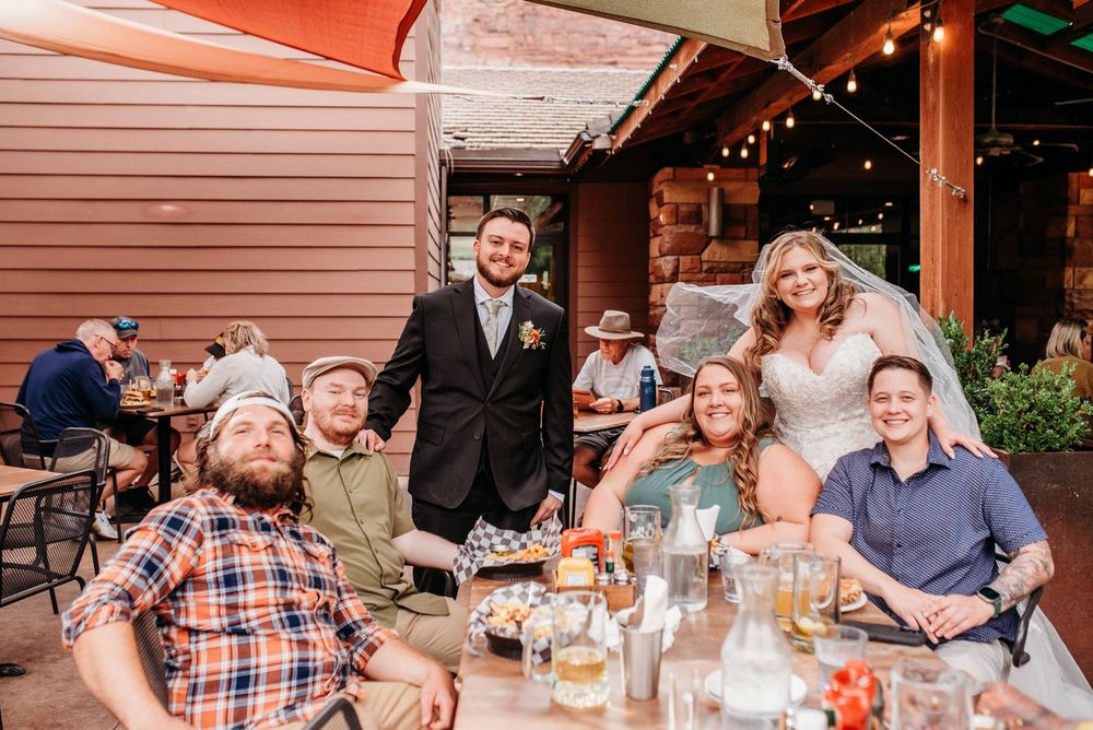 Bride and groom pose with wedding guests at rustic outdoor restaurant reception venue.
