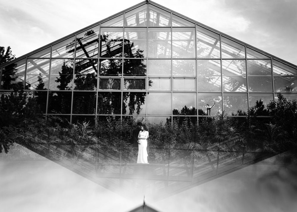 Black and white wedding portrait of a bride in front of a glass greenhouse, by a Calgary wedding photographer
