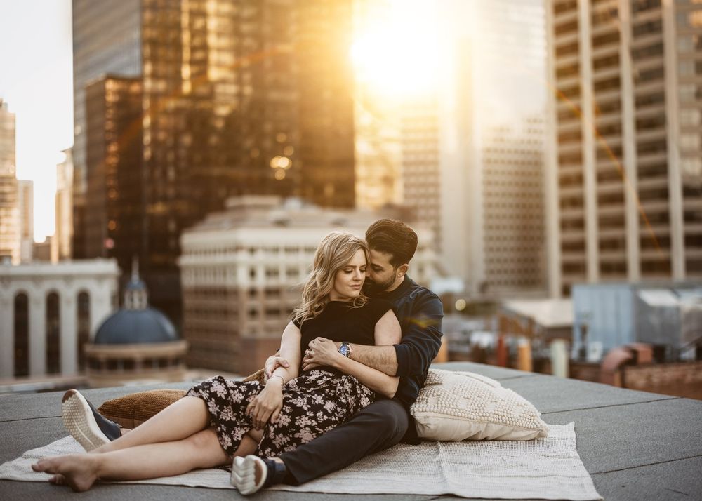Couple lounging together on a city rooftop with warm sun flare, by a Calgary wedding photographer