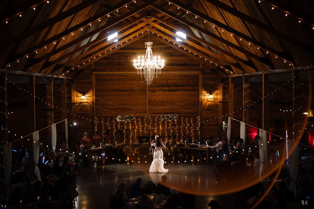 Wide view of a timber hall wedding reception glowing with a chandelier and string lights