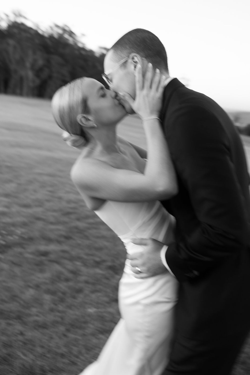 Black and white photo of a bride and groom sharing a romantic kiss outdoors on their wedding day.
