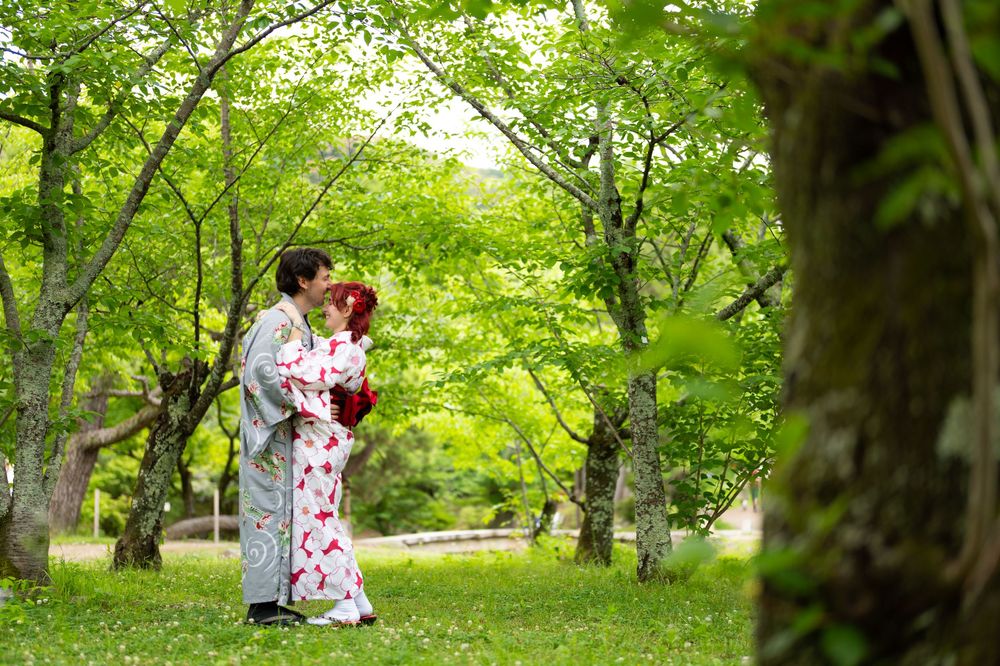 Couple in traditional Japanese kimono sharing a romantic embrace in a lush green forest garden setting.
