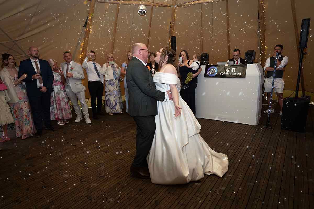 Lucas and Ellie dancing beneath fairy lights inside the tipi at The Den at Four Acre, surrounded by wedding guests.
