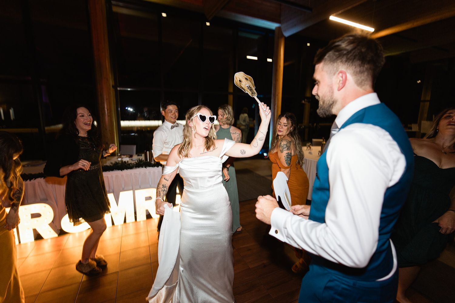 Bride in sunglasses dancing by the lit Mr and Mrs sign at Vista Canmore reception