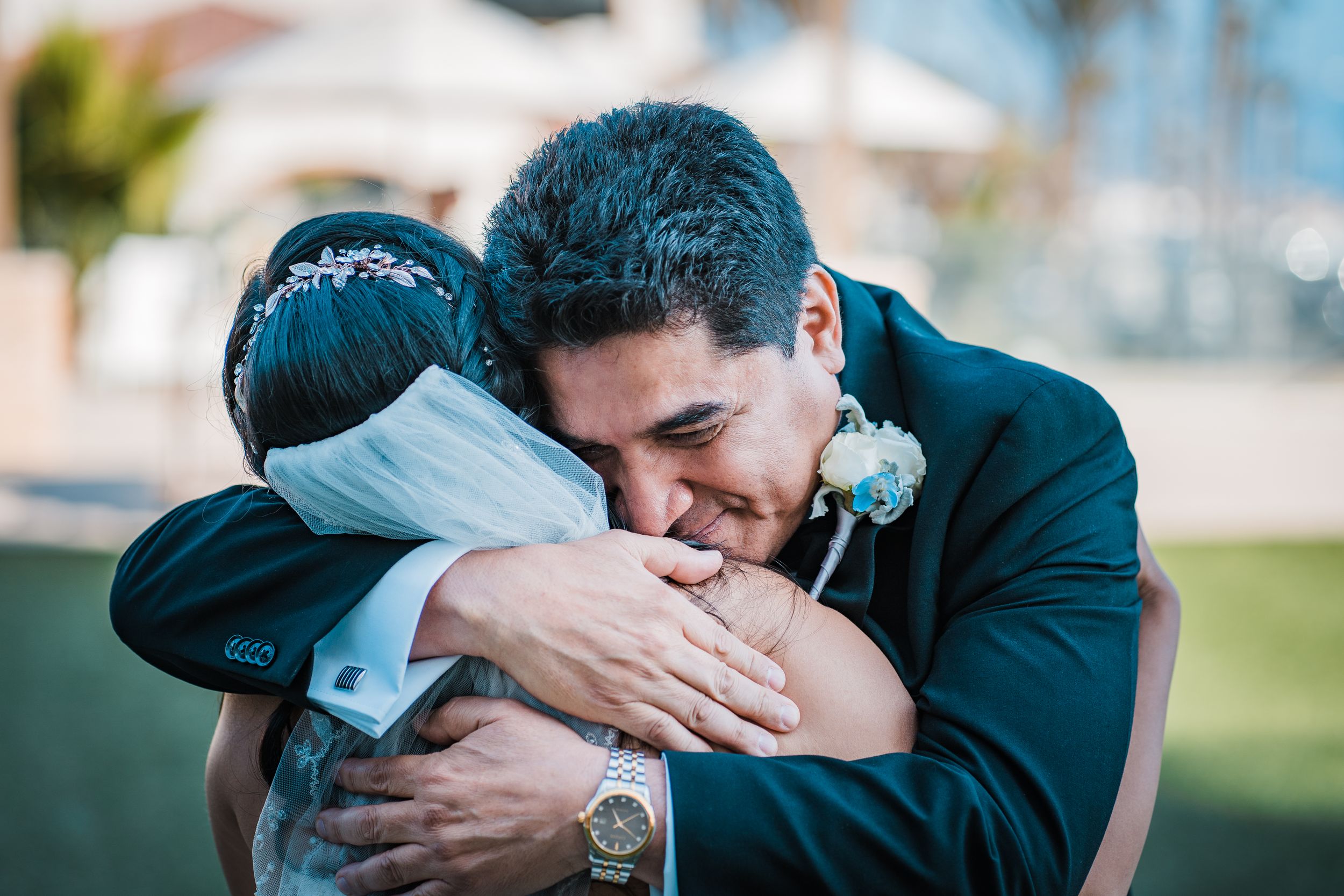 Emotional groom embraces bride in a heartfelt hug during outdoor wedding ceremony celebration.
