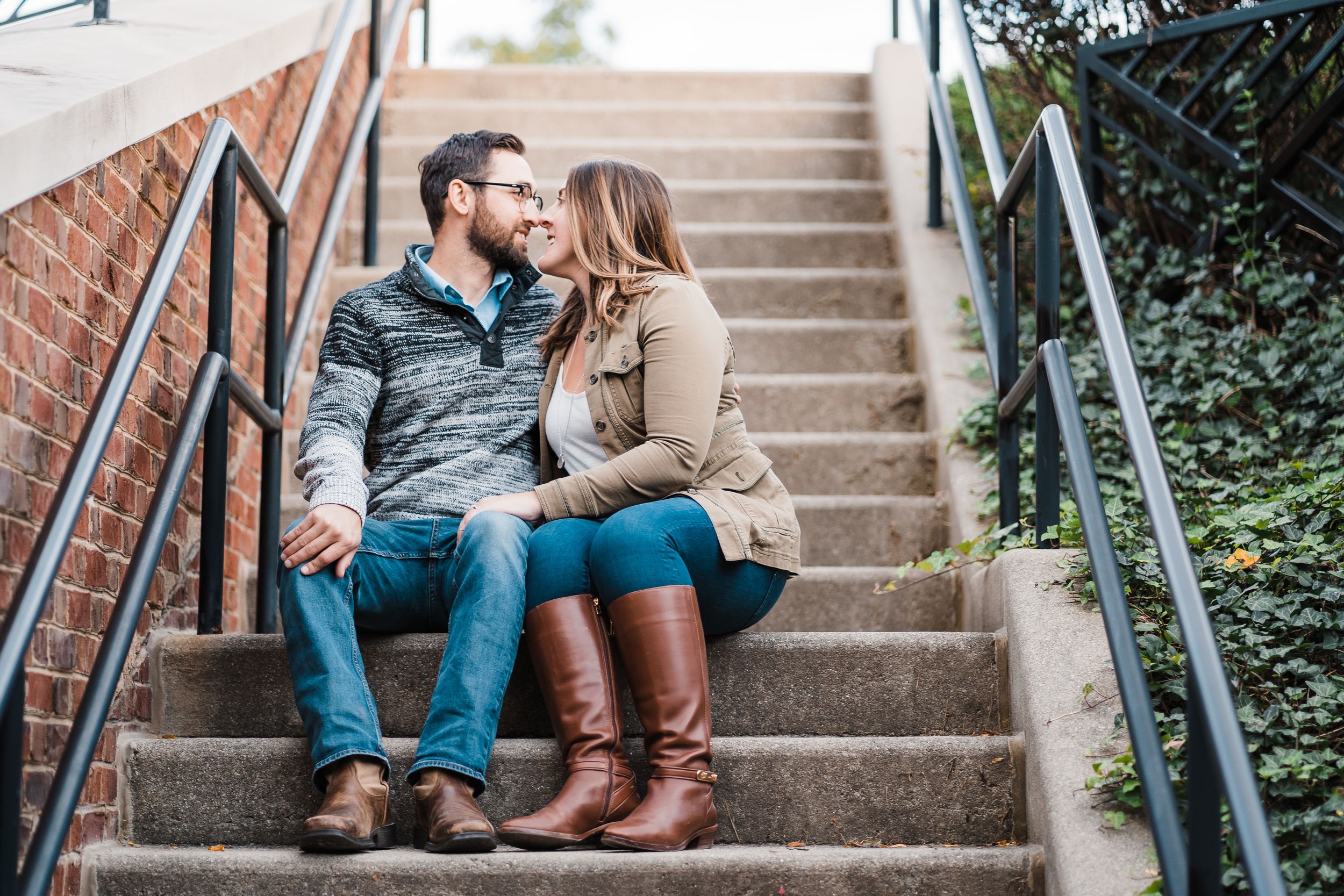Couple sits close together on outdoor brick staircase during a cozy fall engagement photo session.