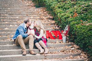 Couple shares a kiss on leaf-covered steps beside a red LOVE sign during fall engagement session.