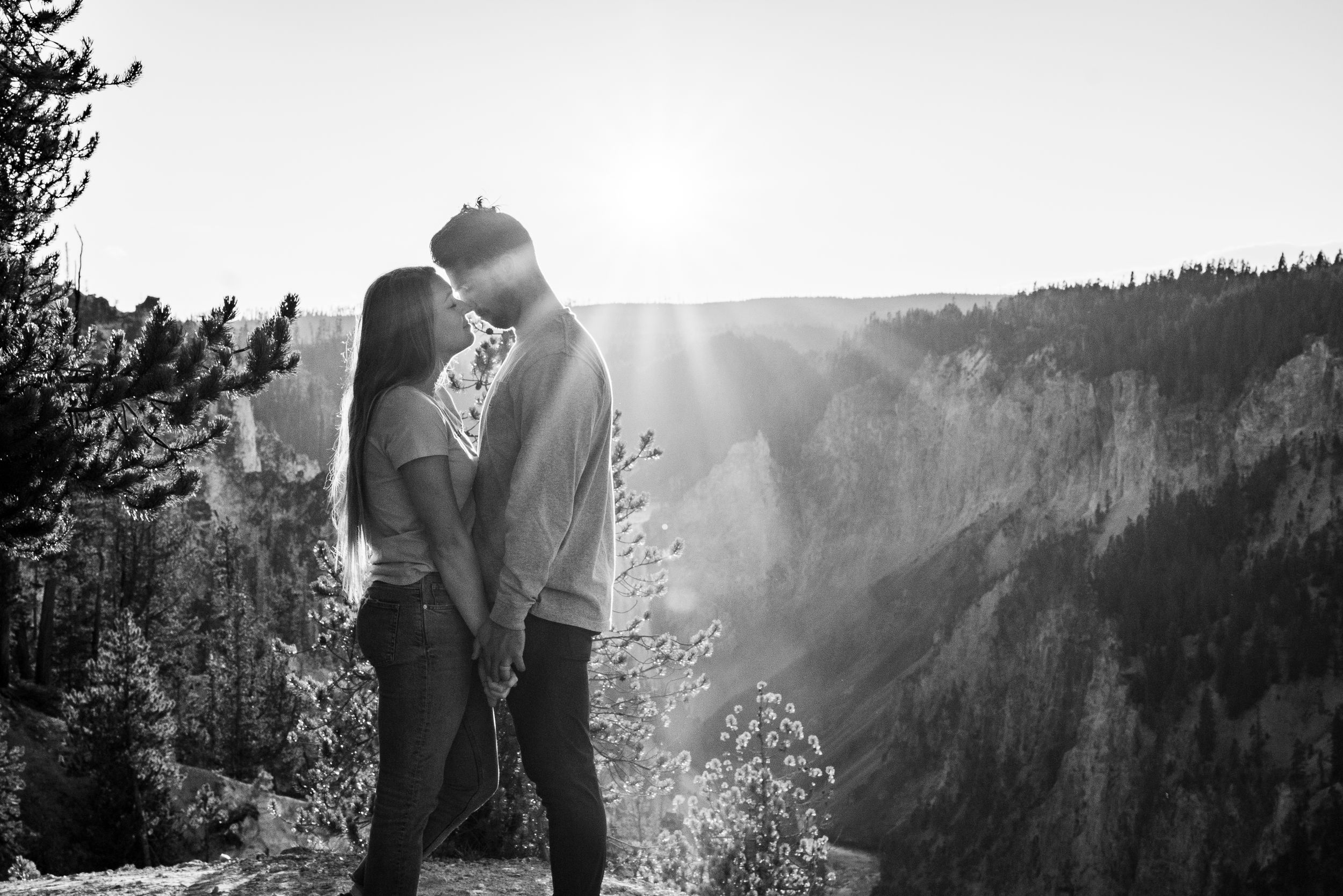 Black and white photo of couple about to kiss on mountain overlook with stunning canyon backdrop.
