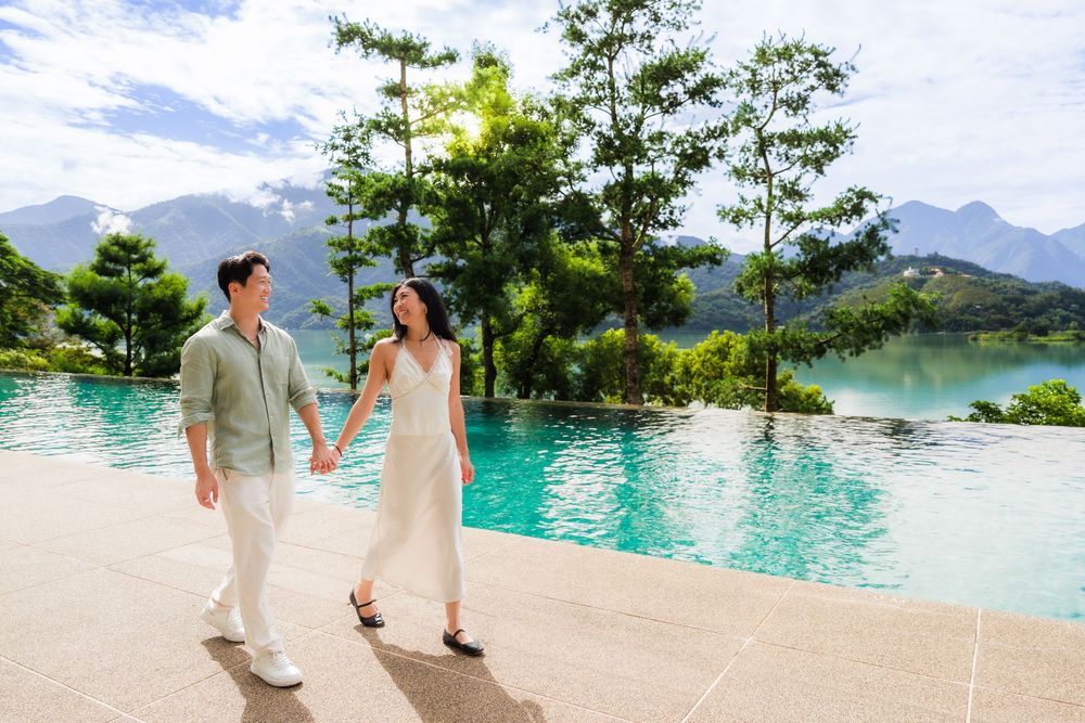 Couple holding hands walking by infinity pool with mountain view.
