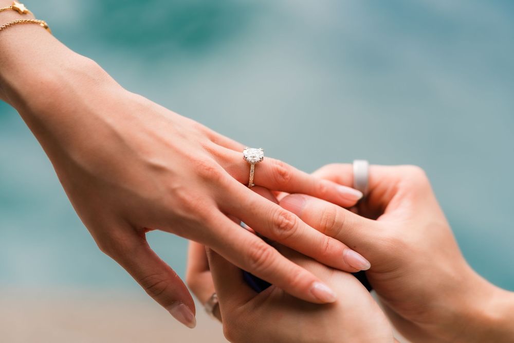 Close-up of a person placing a diamond engagement ring on their partner's finger.