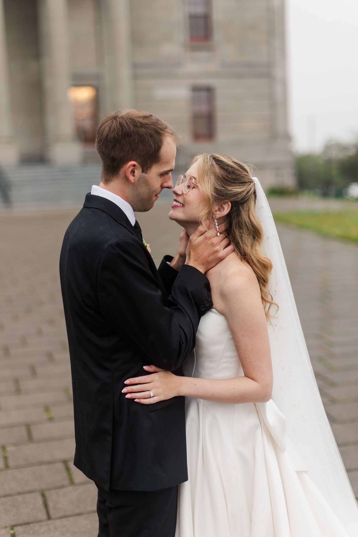 A bride and groom share a romantic moment outside a grand building, with the groom gently holding her face.