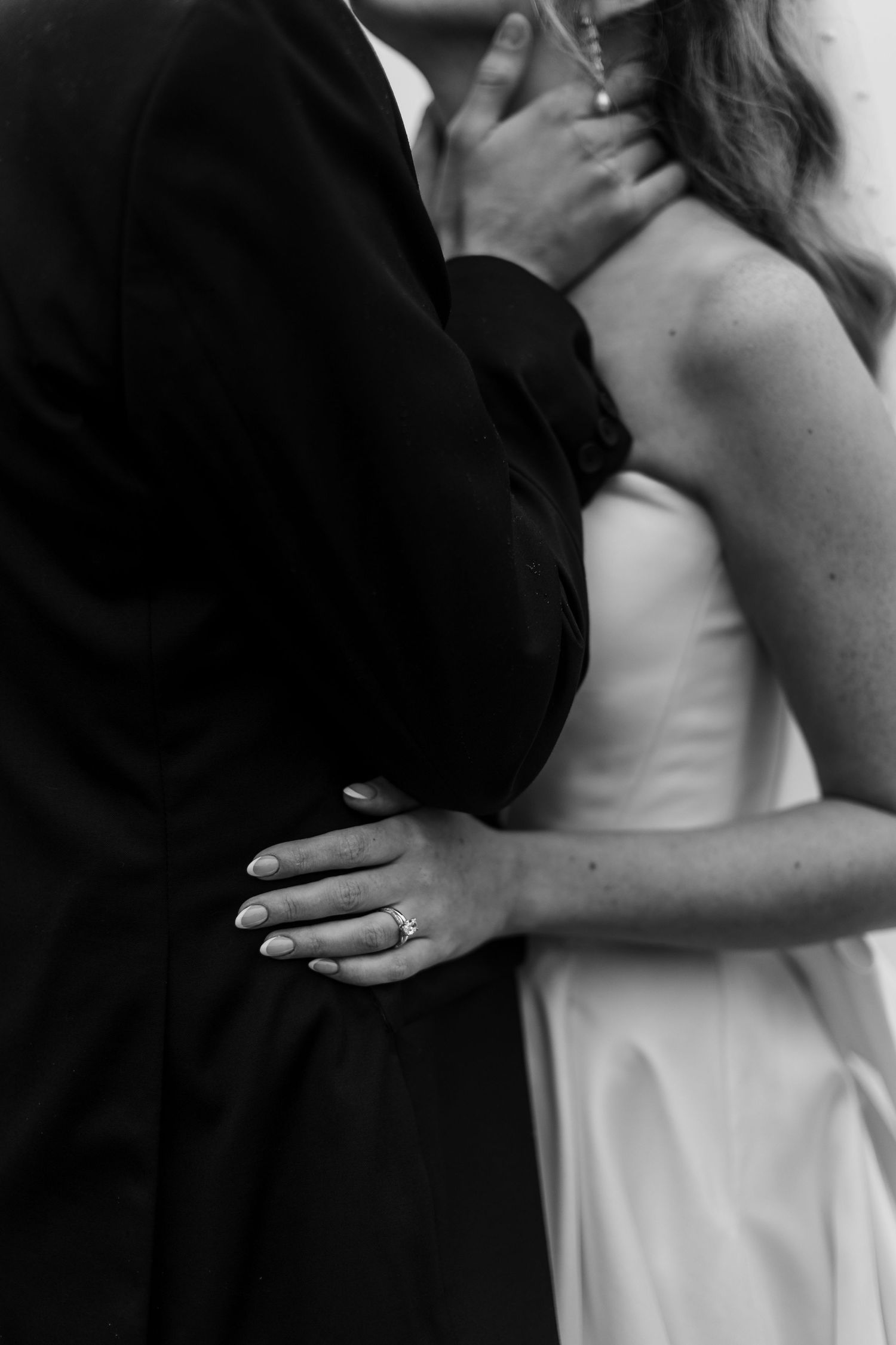 Black and white photo of bride and groom embracing, showcasing diamond engagement ring and wedding dress.