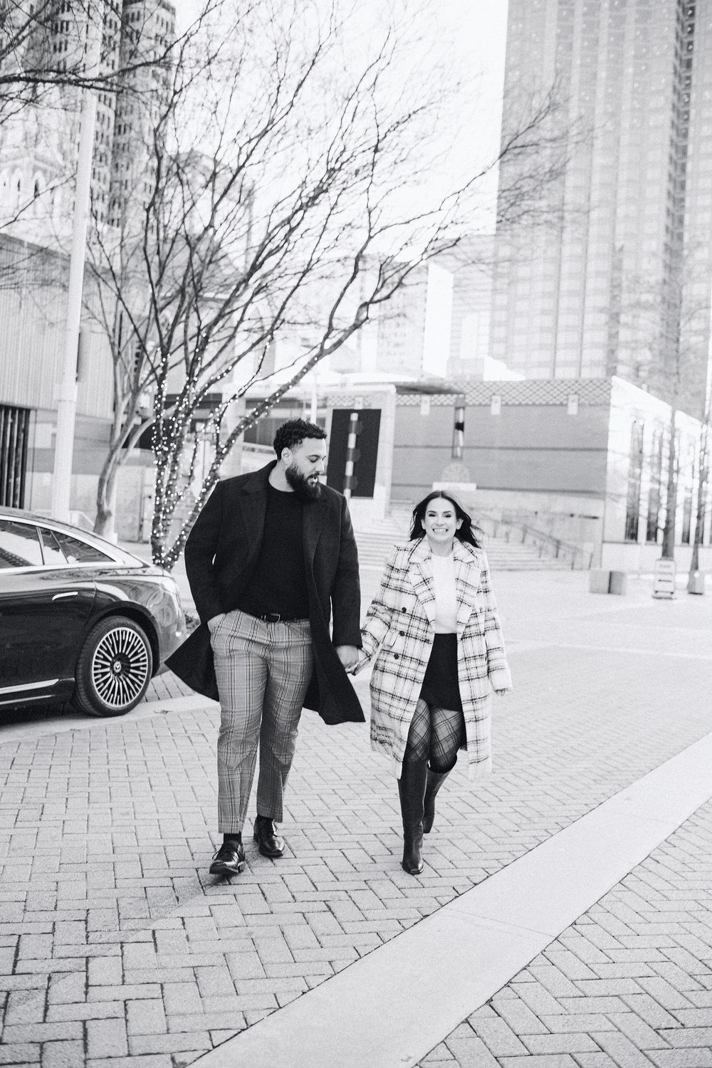 Black and white photo of a stylish couple holding hands and walking together on a city sidewalk in winter coats.