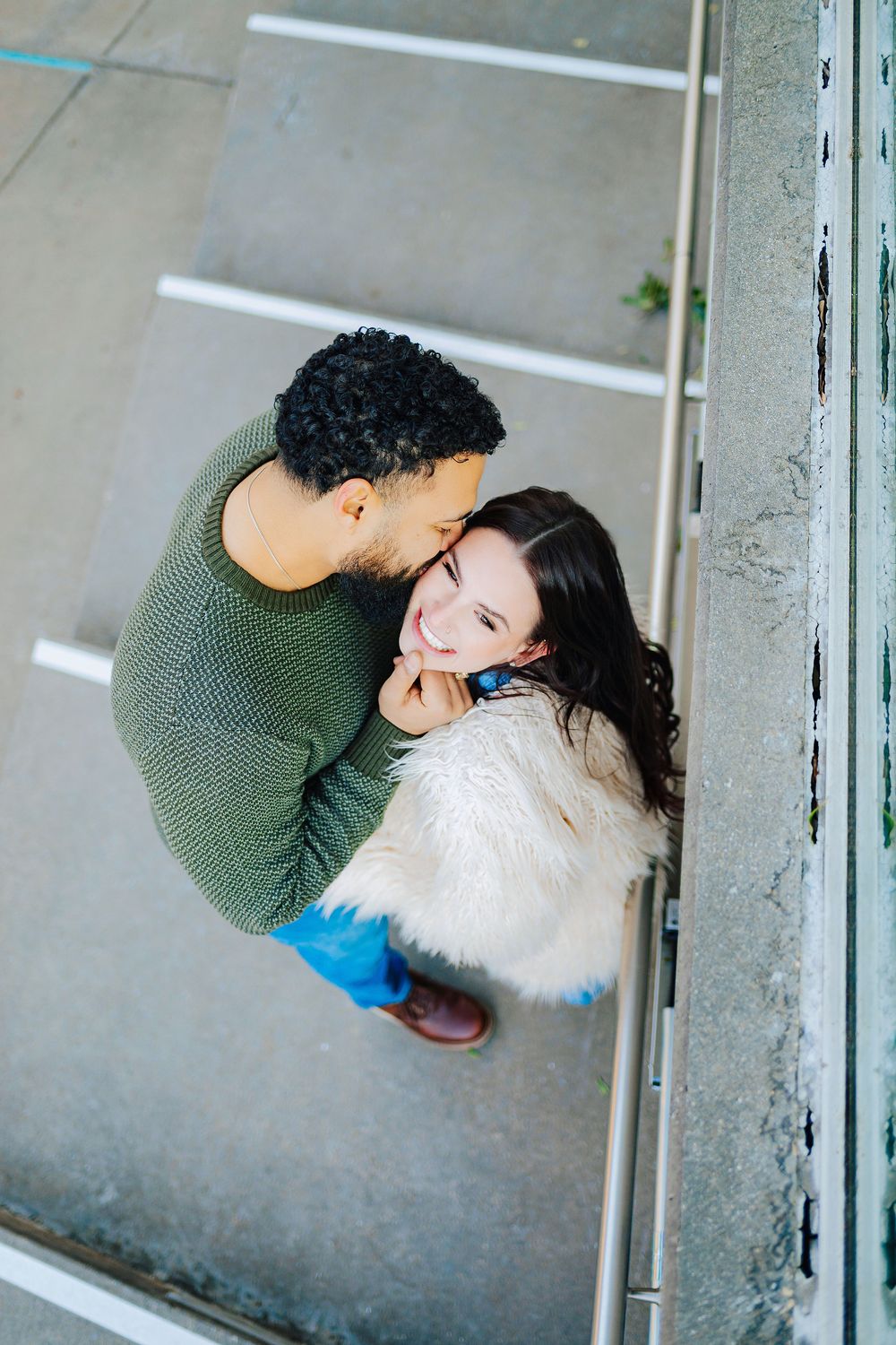 Aerial view of a couple sharing a tender moment, man in green sweater kissing woman in white fur coat on the cheek.