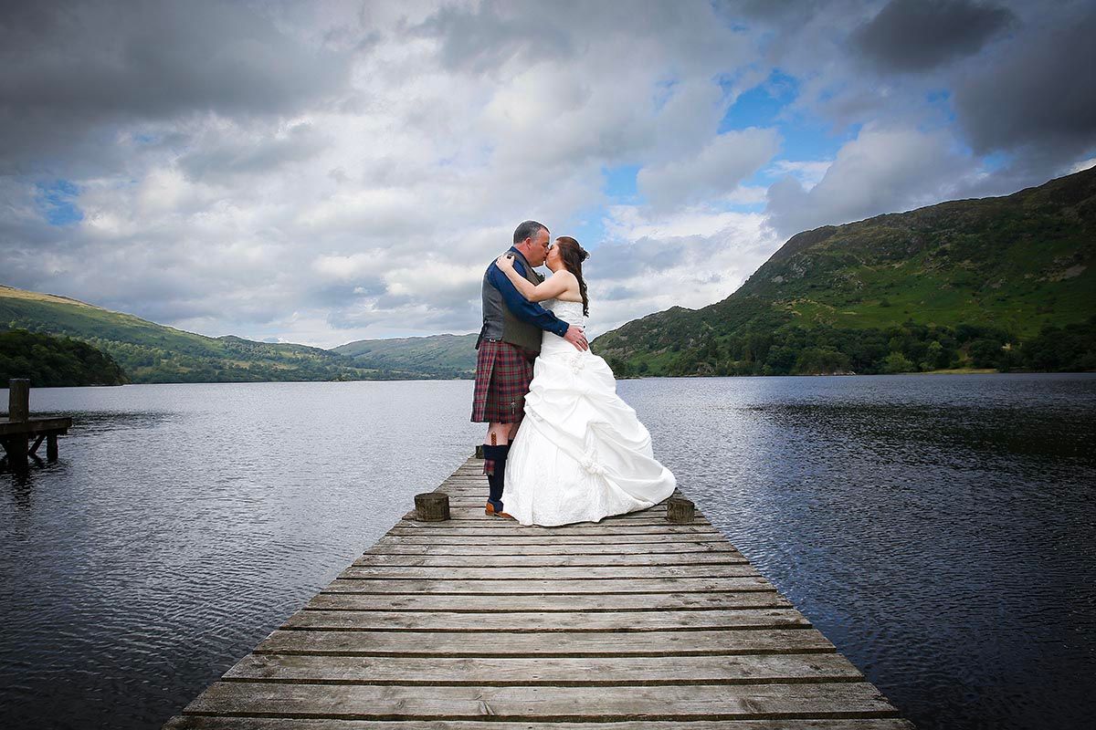 Bride and groom kissing on the iconic jetty at Inn on the Lake wedding venue - Glenridding