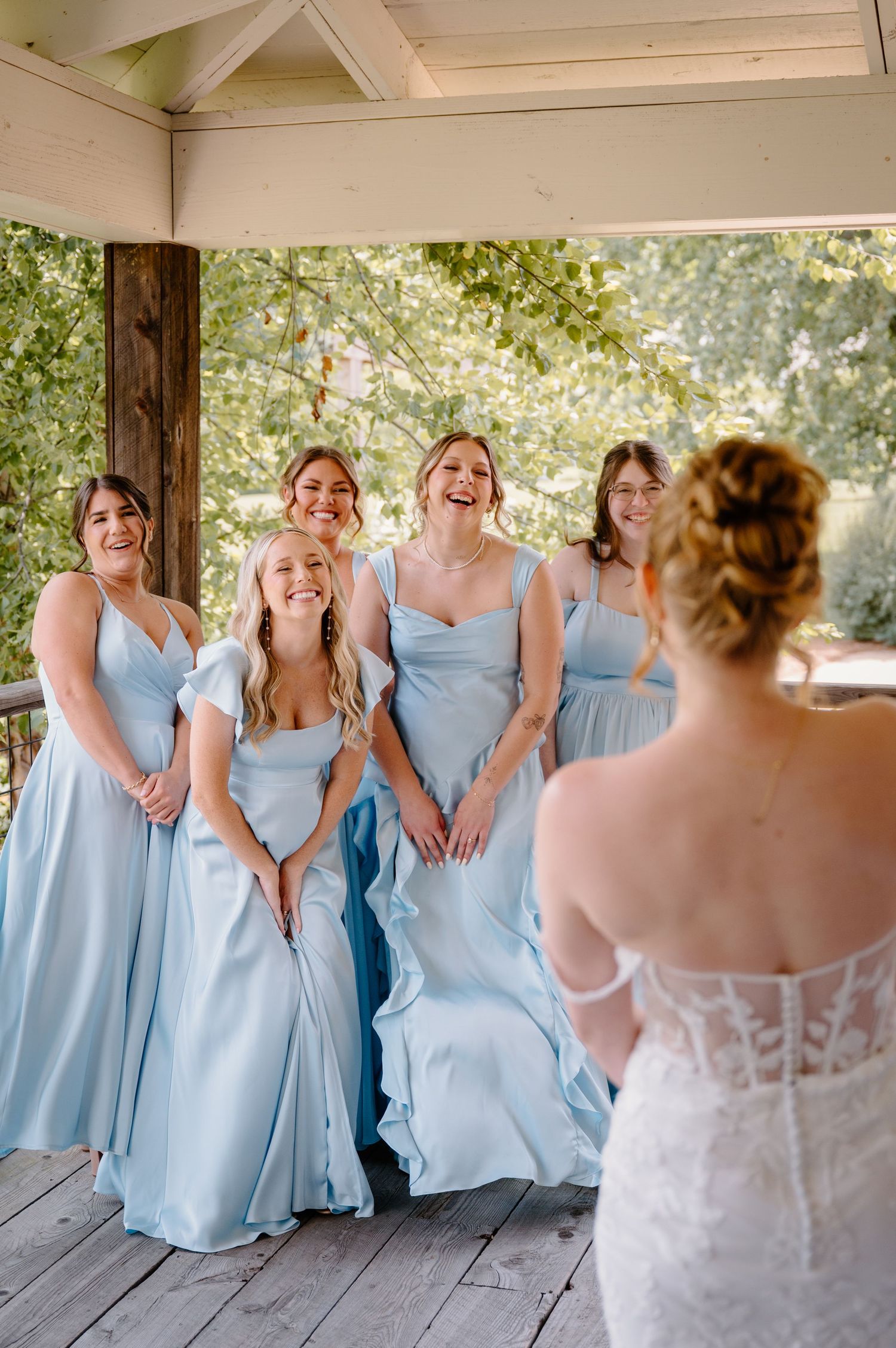 Bridesmaids react with joy seeing the bride in her white lace wedding dress on a wooden deck shot by k Herman Photography