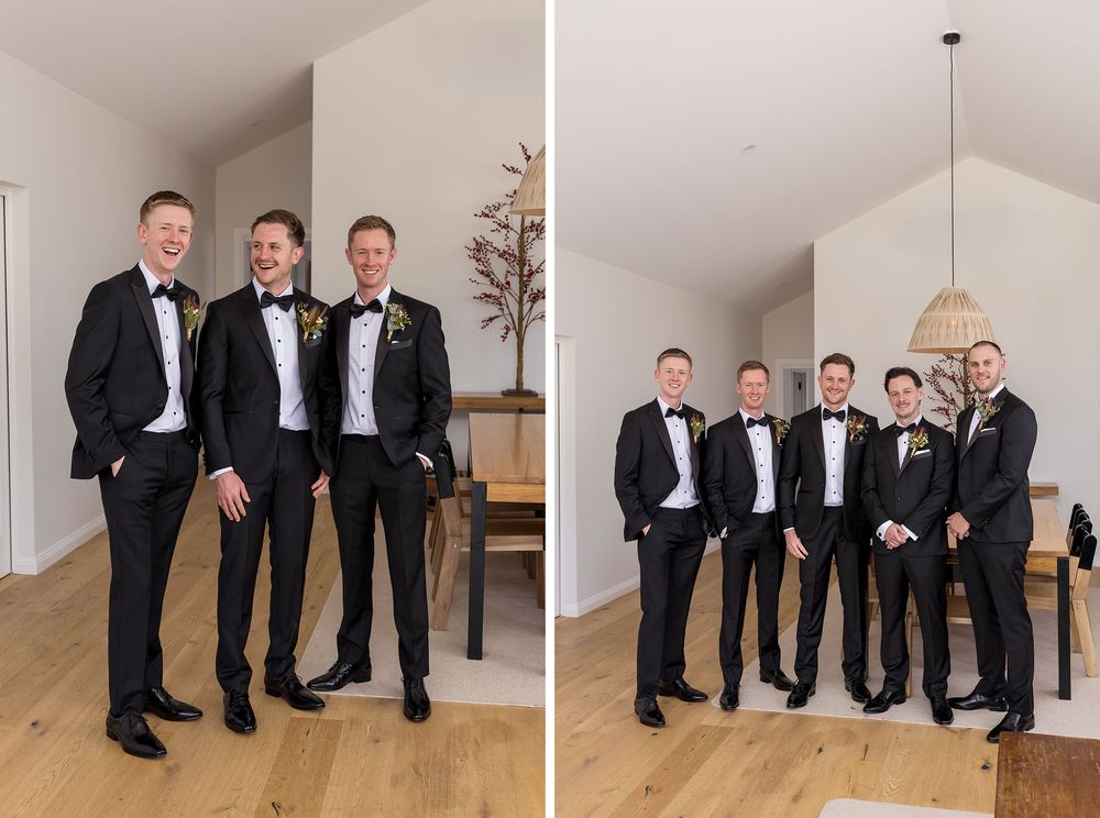 Groomsmen in black tuxedos with bow ties and boutonnieres pose together in a bright, modern room with wood floors and a pendant light.