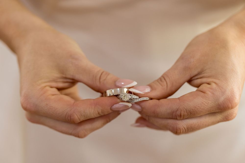Brides's hands with pale pink manicured nails holding a stack of delicate silver wedding rings, some set with sparkling stones.