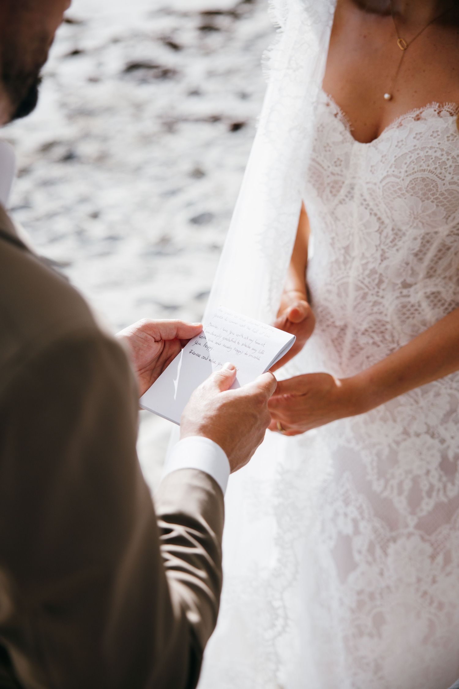 Bride and groom exchanging wedding vows from handwritten cards during a beach ceremony.