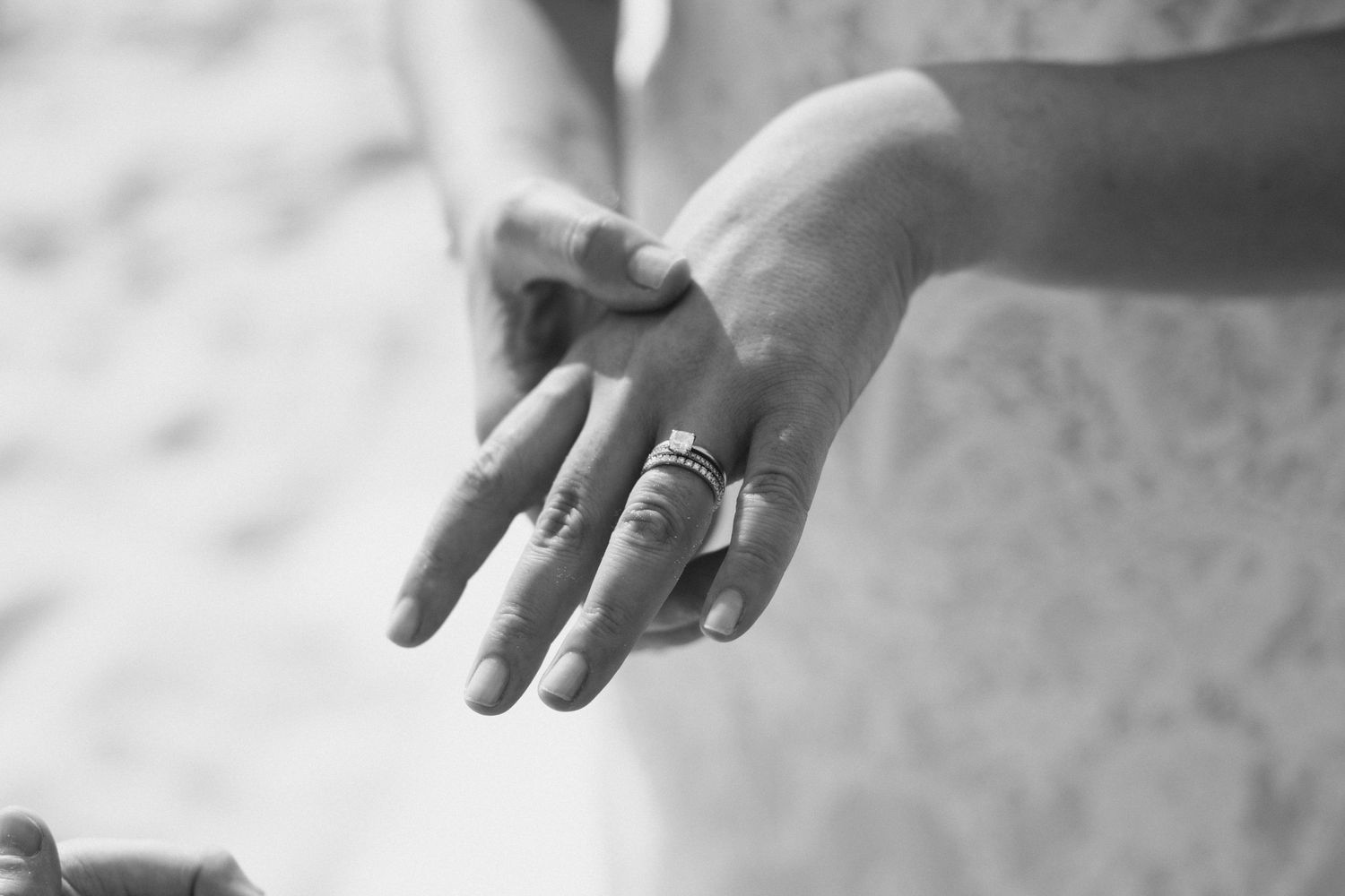 Close-up black and white photo of bride's hands adorned with wedding and stacking rings.