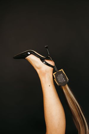 A woman's leg raised high wearing a black patent stiletto heel with a price tag attached against dark background.
