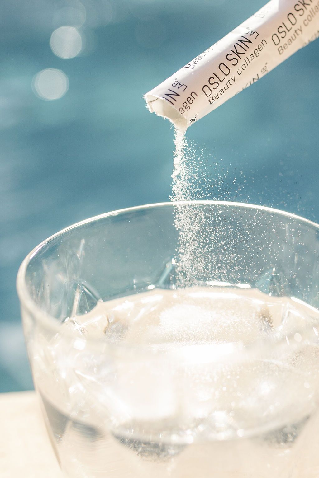 Photographie de la poudre de collagène Oslo Skin Lab répandue dans un verre d'eau devant une piscine
