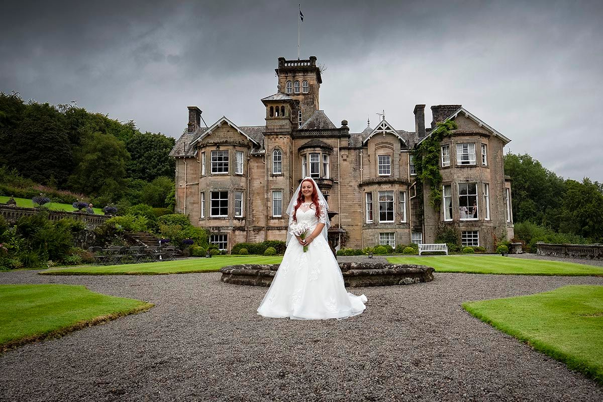 Bride stands in front of Auchen Castle's manicured lawn at southern Scotlands premier wedding venue