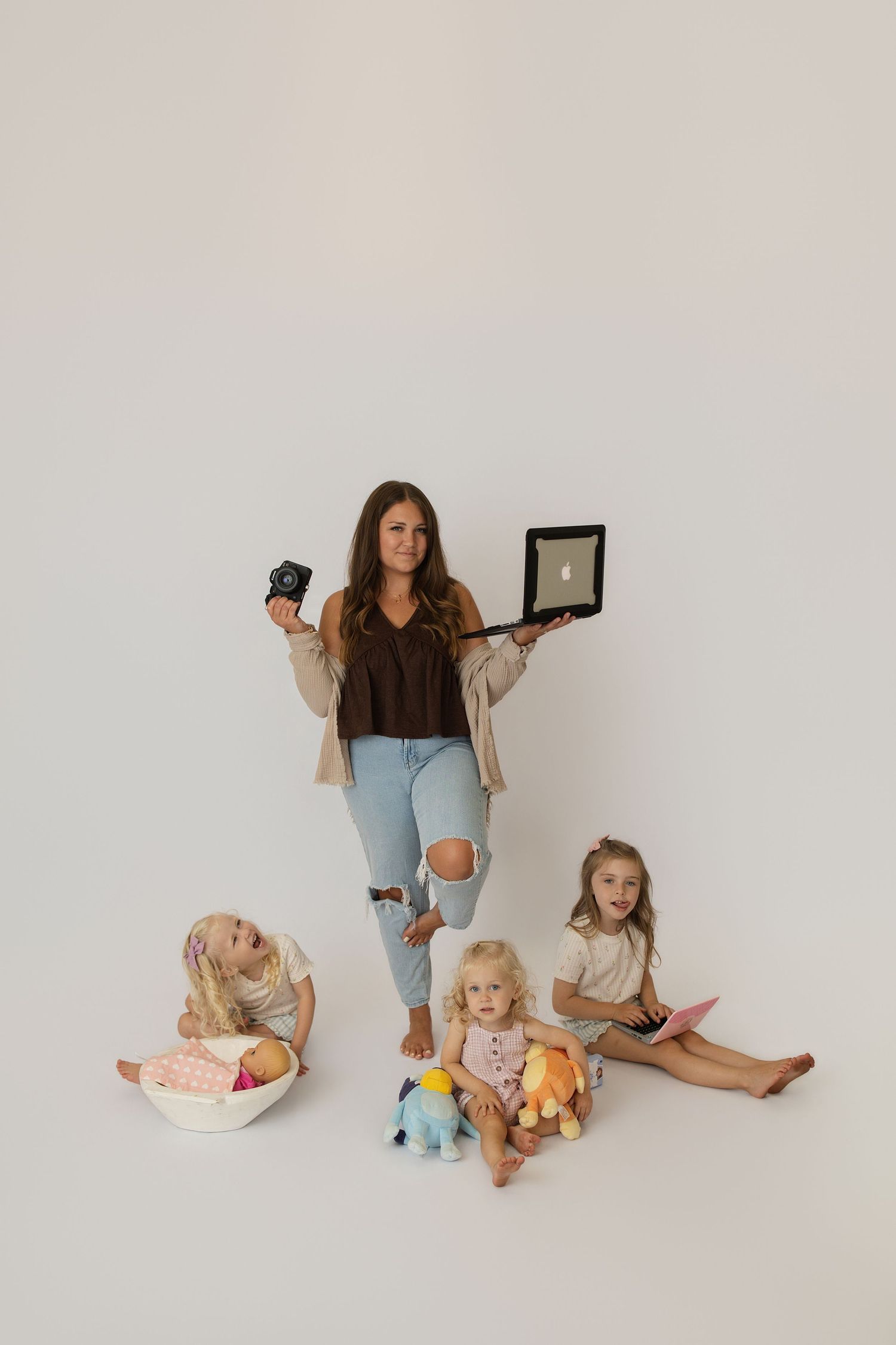 A woman in a trucker hat shows photos to two young girls in a bright indoor studio setting.