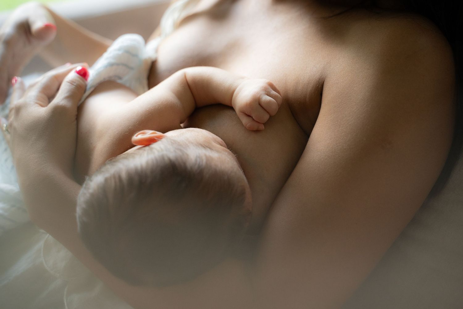 A mother breastfeeding her newborn baby, captured in a soft, intimate close-up photograph.