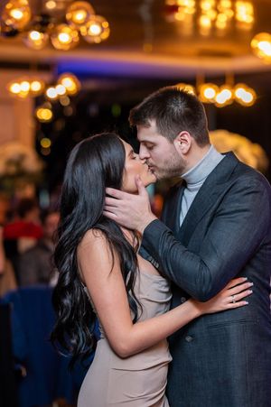 A romantic couple shares an intimate kiss on the dance floor with warm glowing lights in the background.