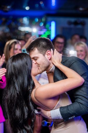 A couple shares a romantic dance at a wedding reception with blue lighting and a crowd in the background.