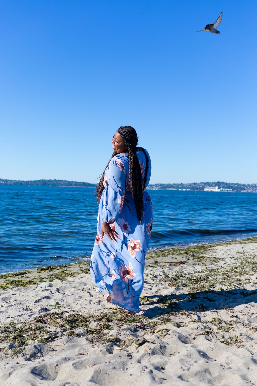 A person wearing a blue floral dress walking towards the water looking back a little.