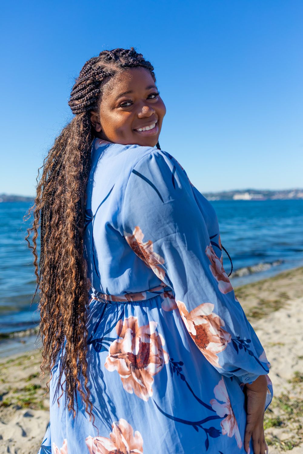 A person wearing a blue floral dress smiling and looking back at the camera.