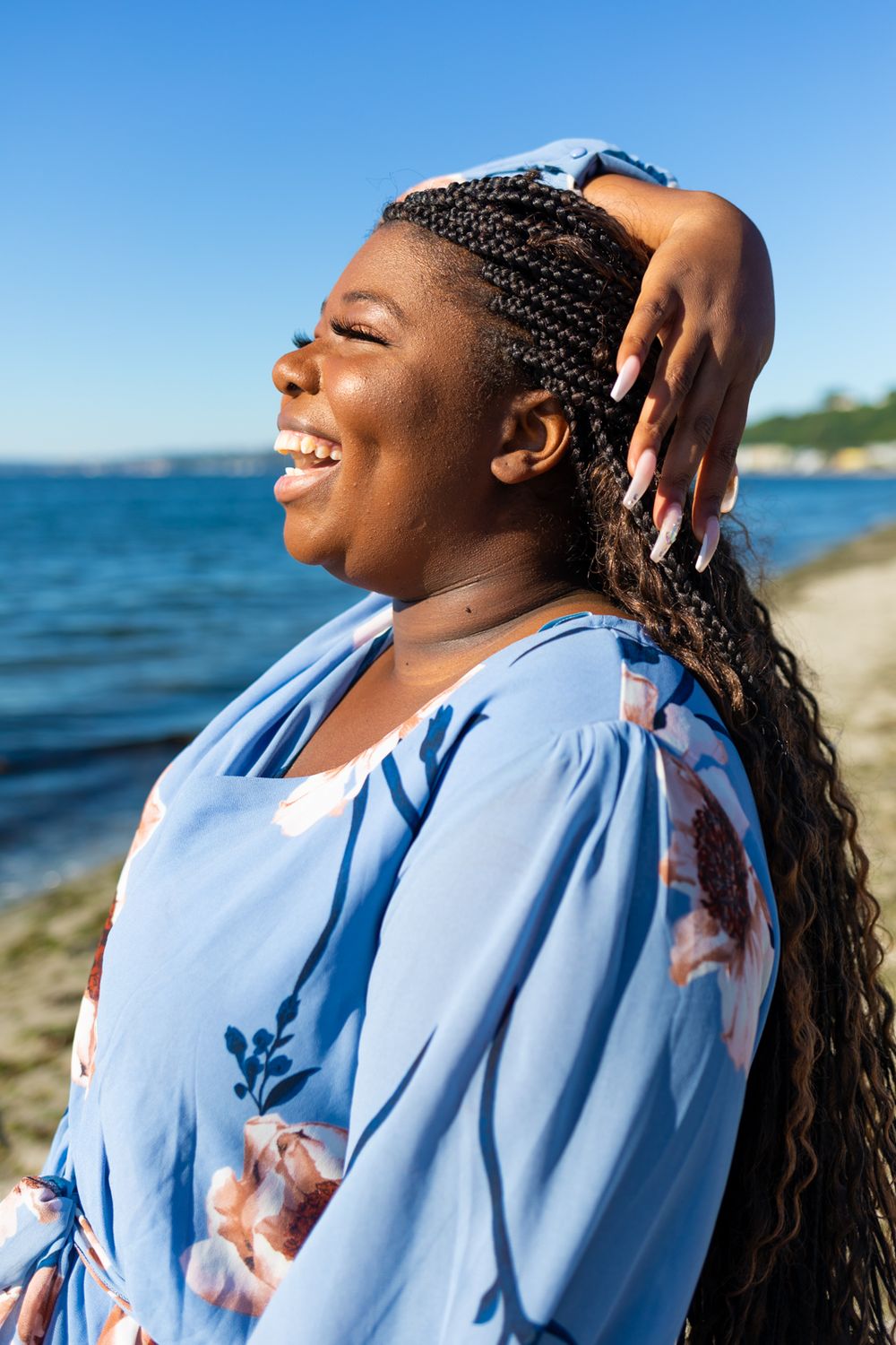 A person wearing a blue floral dress laughing and looking out with her hand near her hair.