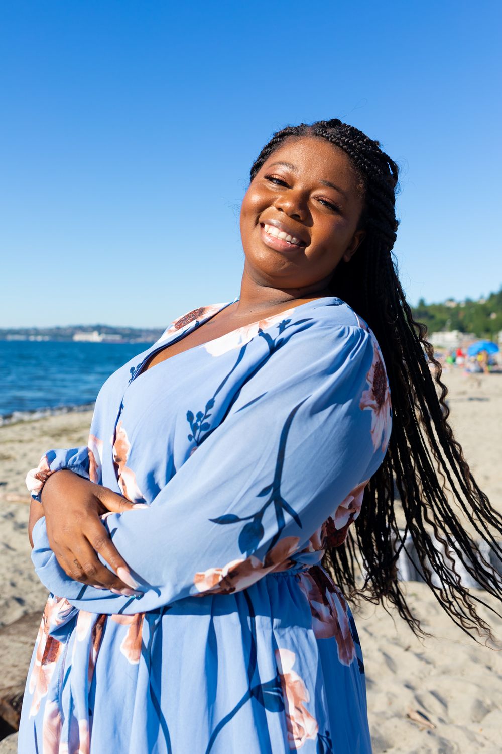 A person wearing a blue floral dress leaning back a little and smiling towards the camera.